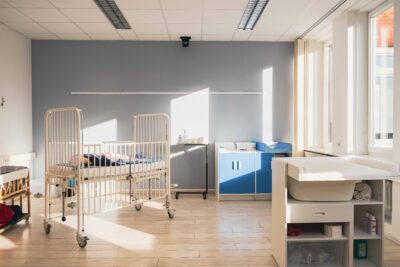 Auf dem Bild sieht man einen Raum mit pflegerischer und medizinischer Ausstattung, einem Wickeltisch und einem Kinderkrankenbett. Das Foto entstand im digitalen Skillslab der ibs Pflegeschule Bremen.